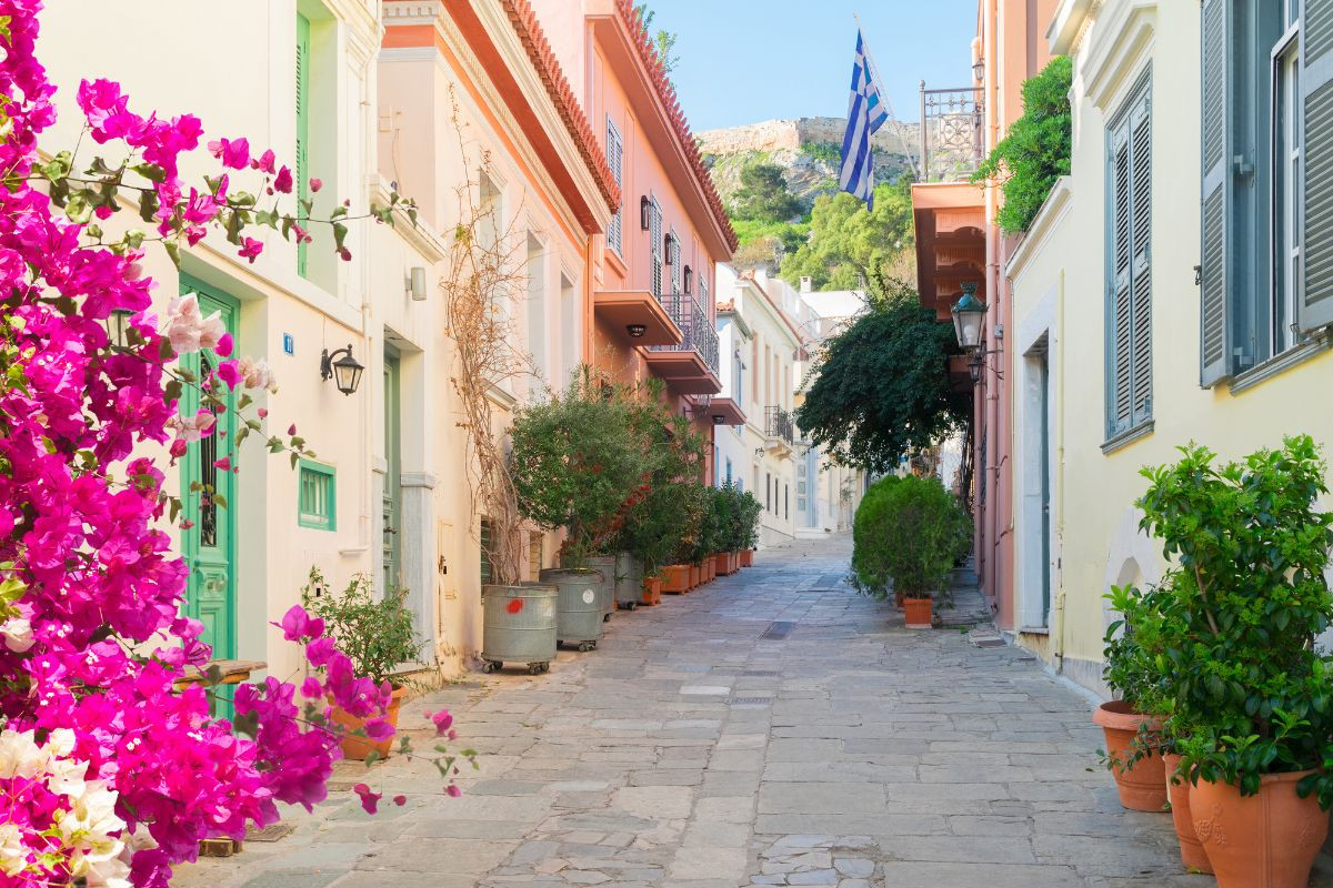 A charming street in Athens, lined with blooming pink bougainvillea and traditional houses, under a clear blue sky.